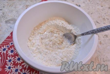 Влить растительное масло и начать частями добавлять тёплую воду, каждый раз полностью вмешивая её. Вначале перемешивать тесто столовой ложкой. Температура воды должна быть не выше 38-40 градусов, если вода будет более горячей, дрожжи могут в ней погибнуть.