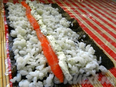 Сворачиваем домашние роллы. Лист нори разрезать пополам, положить на бамбуковую салфетку матовой стороной вверх. На лист нори выложить слой риса, не доходя 1 см до края. Чтобы рис не прилипал к рукам, руки смачивать в воде с уксусом. На рис положить тонкие полоски семги и сливочного сыра.