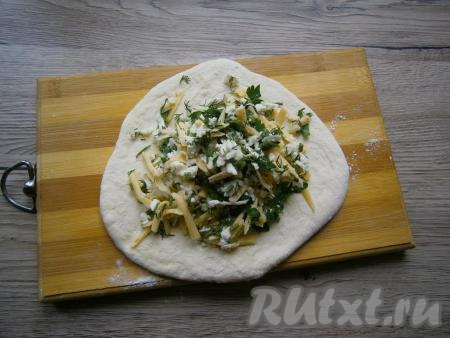 На поверхности, слегка припылённой мукой, раскатать каждый шарик из теста в небольшую лепёшку, в центр которой выложить 1/3 часть начинки из сыра и зелени.