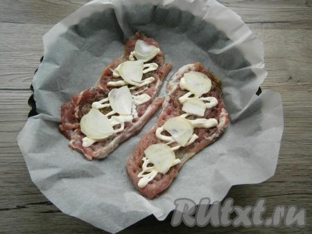 Смазать отбивные сверху майонезом, выложить очищенный и тонко нарезанный репчатый лук.