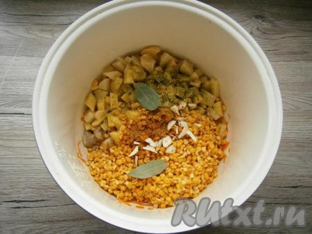 Добавить в чашу к курице и овощам горох и нарезанный кубиками картофель. Всыпать соль, специи, приправу для супа, добавить измельченный чеснок и лавровые листья.