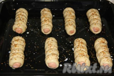 Духовку разогреть. Перед выпеканием смазать сосиски в тесте молочком или водичкой и посыпать кунжутом. Выпекать при температуре 200 градусов, примерно, 25 минут.