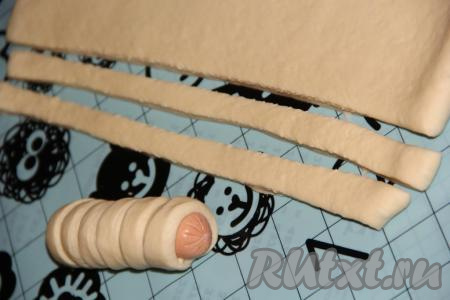 Нарезать тесто на полоски шириной 1 см. Завернуть каждую сосиску в полоску из дрожжевого теста.