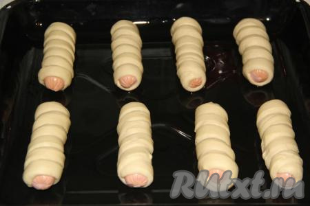 Выложить сосиски в тесте на противень, смазанный растительным маслом, и оставить в тепле на 30-40 минут.