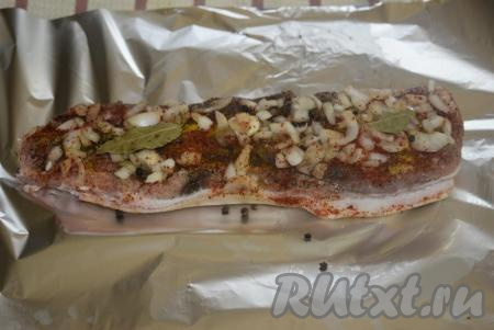 Сверху посыпаем грудинку луком, нарезанным на кубики, черным перцем горошком, выкладываем лавровые листья. Специи, лук и чеснок сделают мясо очень ароматным. Кладем грудинку на фольгу шкуркой вниз, закрываем края фольги плотно и оставляем на 1 час промариноваться.