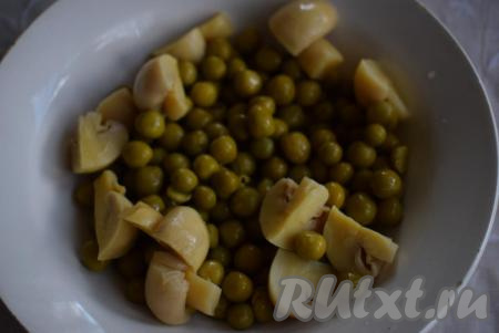 Из банки с зеленым горошком сливаем жидкость, горошек выкладываем в миску. Консервированные шампиньоны режем на крупные дольки и выкладываем к горошку.