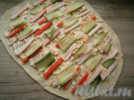 Крабовые палочки нарезать вдоль на 4-5 частей, огурец - тонкими слайсами или брусочками. Разместить крабовые палочки и огурец по всему лавашу горизонтально (как на фото).