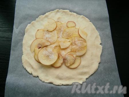 Тесто выложить на лист пергамента и руками растянуть, чтобы получилась тонкая круглая лепешка. Поместить ее вместе с пергаментом на противень. В центр лепешки выложить 2-3 слоя яблок, посыпая каждый слой сахаром и корицей. 