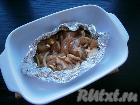 Из фольги, сложенной вдвое, сделать лодочку, влить в нее растительное масло и выложить кусочки куриного филе с луком. Лодочку поместить в небольшую форму для запекания или на противень.