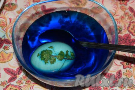 Перевязываем капрон резиночками или нитками (это делается для того, чтобы закрепить капрон на яйце). Опускаем яйцо с растением в миску с красителем и аккуратно ложкой поливаем его со всех сторон, периодически переворачивая его со стороны на сторону (я держала яйцо в красителе не более 1 минуты, чтобы оно получилось не очень ярким, следуя своей задумке - сделать яйца голубого цвета).