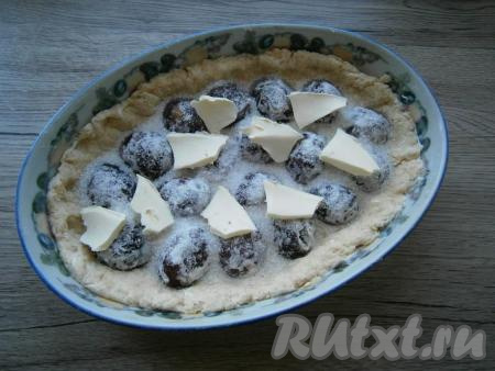 Достать тесто из духовки, выложить сливы срезами вниз в один ряд. Посыпать сливы сахаром и выложить сверху кусочки сливочного масла.