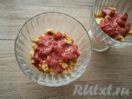 В креманки выкладывать десерт в несколько слоев. Вначале нужно раскрошить печенье (совсем мелко крошить не нужно), немного полить ягодным соусом.