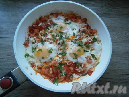Накрыть сковороду крышкой и на слабом огне прожарить яйца около 2-3 минут, но так, чтобы желтки остались жидковатыми. Готовую яичницу "Шакшука" посыпать измельченным чесноком и зеленью петрушки.