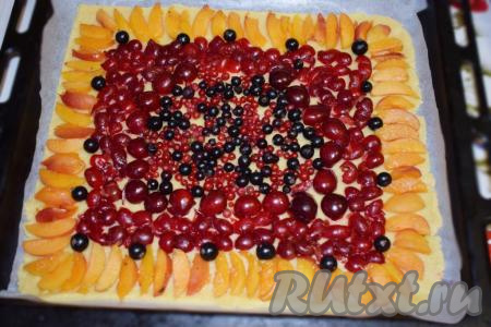 Перекладываем пергамент с тестом на противень. Раскладываем ягоды. Я решила ягоды черной и красной смородины выложить по центру пирога, затем по кругу разложила ягоды черешни, предварительно очищенные от косточек, затем разложила вишню, удалив из неё косточки, обрамила песочный пирог абрикосами, нарезанными на дольки.