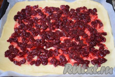 Перекладываем пергамент с тестом на противень, выкладываем вишневую начинку, равномерно распределяя ее по поверхности теста, оставляя края чистыми.