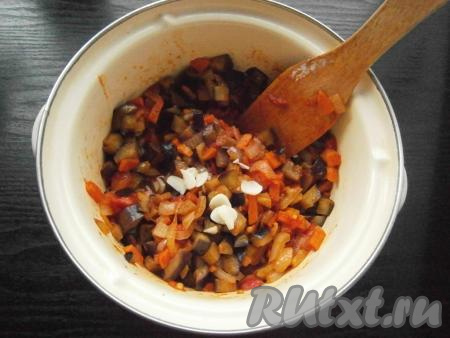 Влить немного горячей воды, перемешать и протушить овощи 5 минут на небольшом огне, после чего выложить их в кастрюлю к баклажанам. Сюда же влить оставшуюся воду и добавить измельченный чеснок.