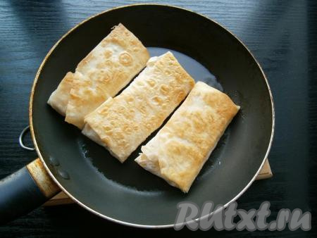 Жарить конвертики из лаваша с колбасой и сыром на небольшом огне до румяности, после чего перевернуть и также обжарить до румяного цвета.