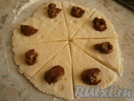 Далее тесто нужно разделить на 2 части. На столе, присыпанном мукой, каждую часть теста раскатать в лепешку толщиной около 0,5-1 см, разрезать на 8 сегментов. На край каждого сегмента поместить по чайной ложке начинки из вареной сгущенки, повидла или выложить по несколько свежих ягод или фруктов.