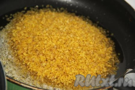 В другую сковороду влить 50 грамм оливкового (или растительного) масла, всыпать булгур. Жарить крупу в масле на среднем огне, постоянно помешивая. Вы увидите, как начнёт меняться цвет булгура.