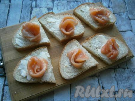 Обрезь семги сформировать в виде розочек (если рыба куском, вначале порежьте ее на тонкие слайсы, а потом сделайте розочки). Розочки разместить на каждом ломте батона ближе к краю.