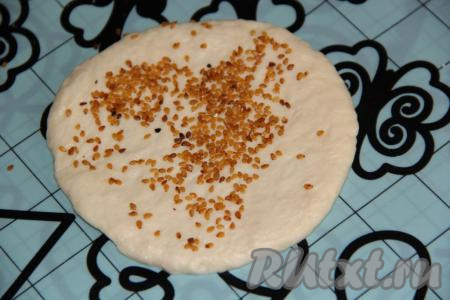 Посыпать каждую лепёшку кунжутом и вкатать его скалкой в тесто с двух сторон.