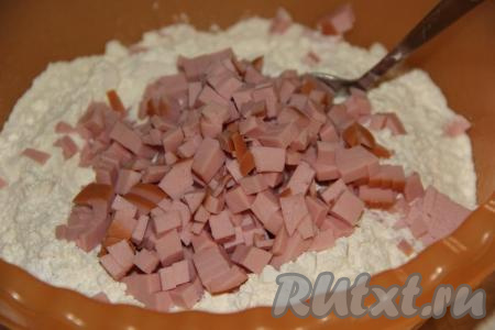 Муку насыпать в глубокую миску, добавить нарезанную колбасу.
