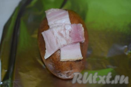 Далее берем фольгу и кладем на нее картофель (для каждого клубня нужен отдельный кусок фольги), на крестообразный надрез выкладываем 2 полоски сала (как на фото).