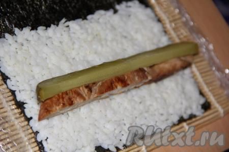 Я листы нори не разрезала, готовила роллы на целом листе. Лист нори блестящей стороной вниз выложить на циновку. Небольшое количество риса равномерно распределить по 2/3 поверхности листа, а, примерно, 1/3 листа оставить чистой. Выложить на рис брусок куриного филе и брусочек огурца (как на фото).