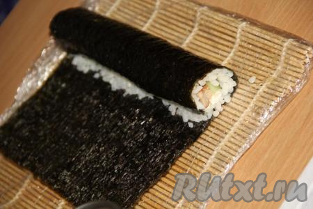 Свернуть лист с начинкой в плотный рулет. Край листа нори, на котором нет риса, смазать водичкой, так он хорошо склеится и ролл получится плотным и красивым.