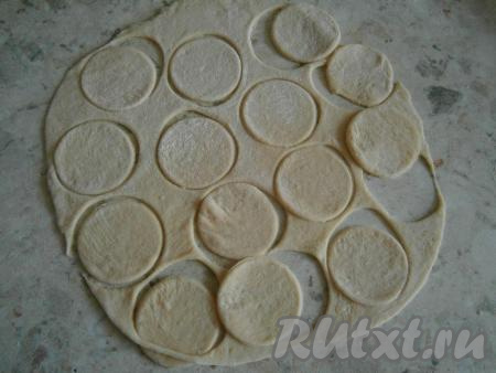 Тесто обмять, разделить его на 2 части. На присыпанном мукой столе раскатать каждую часть теста в тонкую лепешку. Рюмкой вырезать кружочки.