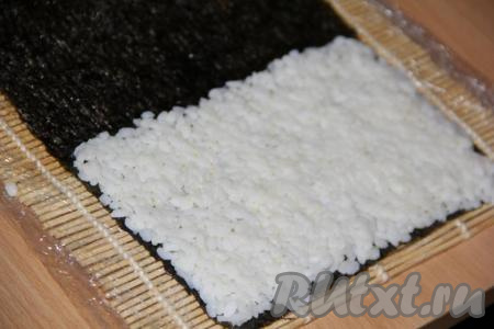 Приступаем непосредственно к приготовлению роллов в домашних условиях. Я использовала целый лист нори, роллы получились не маленькими, но очень ровными и красивыми.&nbsp;Лист нори блестящей стороной вниз выложить на циновку. На 2/3 листа нори выложить небольшое количество риса и равномерно его распределить. Оставить чистой, примерно, 1/3 листа.&nbsp;