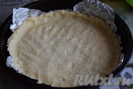 Делим тесто на 2 неравные части: большая часть теста станет основой выпечки, а меньшую часть будем использовать для покрытия верха пирога. В форму диаметром 24 см выкладываем фольгу (или пергамент) и равномерно распределяем большую часть теста по всему периметру формы, формируя бортики.