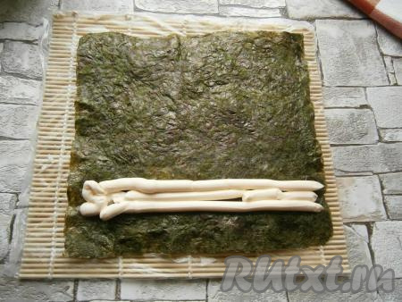 Ближе к нижнему краю листа нори выдавить 2-3 полоски сливочного сыра, выложив его предварительно в кулинарный мешок с обрезанным концом.