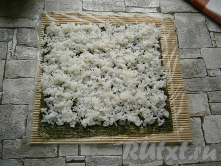 На циновке расположить лист нори шершавой стороной кверху. Разложить на нем слой риса, не доходя до нижнего края листа около 1 см (как на фото).