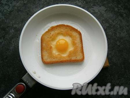 Обжарить хлеб на среднем огне до румяности с одной стороны, перевернуть. Вбить в серединку сырое яйцо, огонь сделать минимальным, прикрыть сковороду крышкой.