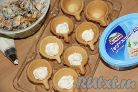 Творожный сливочный сыр переложить в кондитерский мешок (выкладывать сыр в тарталетки с помощью кондитерского мешка очень удобно, но можно выложить и ложкой) и отсадить в каждую тарталетку (сыр должен закрыть дно тарталеток, как на фото).