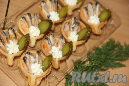 Выложить в каждую тарталетку по 3 мидии, слегка вдавливая их в сыр. Огурчик нарезать тонкими кружочками и добавить в тарталетку. Зелень можно мелко нарезать и посыпать мидии, а можно вставить веточки укропа в сыр. У меня осталось немного сыра и я в каждую тарталетку с мидиями выложила с помощью кондитерского мешка сыр в виде маленького цветочка.