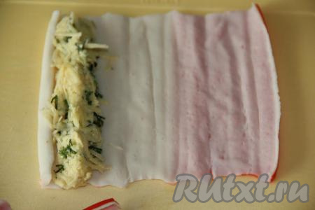 Выложить немного начинки на край крабовой палочки по всей длине (как на фото).