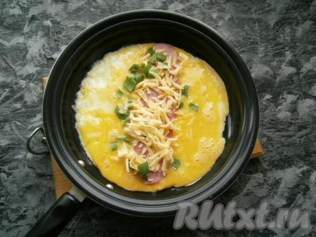 Вылить яйца на разогретую с растительным маслом сковороду. По центру выложить ломтики колбасы, посыпать их сыром и измельченным зеленым луком. Прикрыть сковороду крышкой и на медленном огне довести яичницу&nbsp;до тех пор, пока она&nbsp;сверху не перестанет быть жидкой.