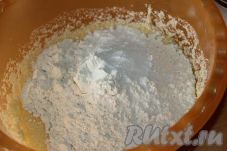 Затем всыпать разрыхлитель, небольшими порциями начать добавлять муку, вначале перемешивая тесто столовой ложкой, а как только тесто начнёт собираться в ком, продолжать замешивать его руками.