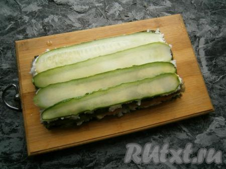 Далее распределить по листу второй стакан риса, смазать сыром, выложить слайсы из огурца.