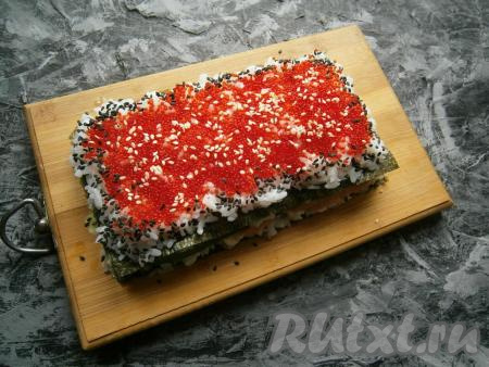 Сверху покрыть торт икрой тобико, не доходя до краев по 1 см. Края суши-торта посыпать черным кунжутом, а саму икру присыпать белым кунжутом.