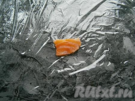 Семгу нужно нарезать на нетолстые кусочки размером, приблизительно, 2х4 см. Отрезать кусок пищевой пленки размером 25х25 см, разместить ее ровненько на поверхности стола, в центр пленки&nbsp;выложить кусочек семги.