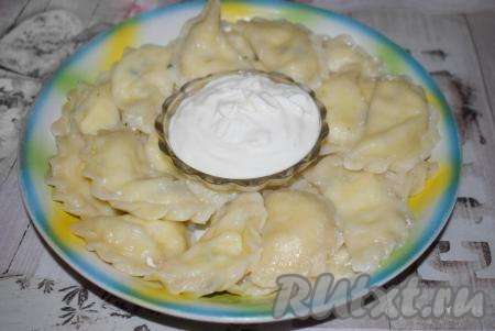 Готовые вареники с творогом и зелёным луком достаём из кастрюли при помощи шумовки, выкладываем на блюдо, смазываем сливочным маслом и подаем к столу горячими со сметаной.