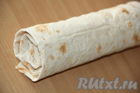 Завернуть края лаваша с двух сторон. Затем свернуть лаваш с начинкой в плотный рулет. Рулет из лаваша завернуть&nbsp;в пищевую плёнку (или фольгу) и убрать в холодильник минут на 40.