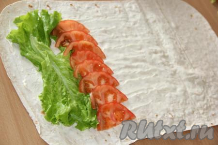 Листья салата промыть под водой и обсушить. Помидор вымыть и нарезать на тонкие полукружки. Разместить на краю лаваша 2-3 листа салата, затем выложить полоской помидоры.