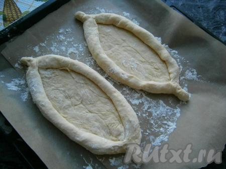 Каждую часть теста раскатать в овал толщиной около 0,5 см и завернуть края (как на фото), формируя лодочку. Концы теста с двух сторон каждой "лодочки" скрутить. Противень застелить пергаментом, немного посыпать мукой и разместить "лодочки".