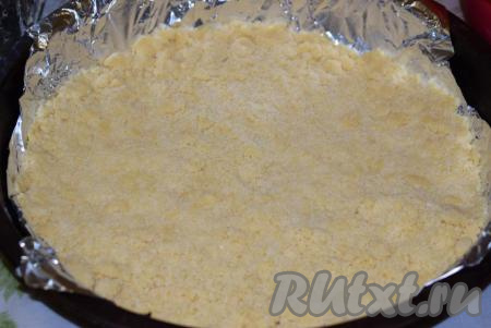 Дно формы (у меня форма диаметром 28 см) застилаем фольгой (или пергаментом), затем насыпаем 2/3 крошки из теста. Разравниваем крошку руками, плотно надавливая на неё.