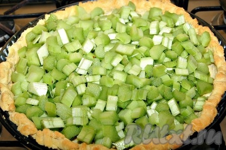 Вытащить из духовки испеченный до полуготовности песочный корж и выложить на него нарезанный ревень, посыпанный  сахаром.