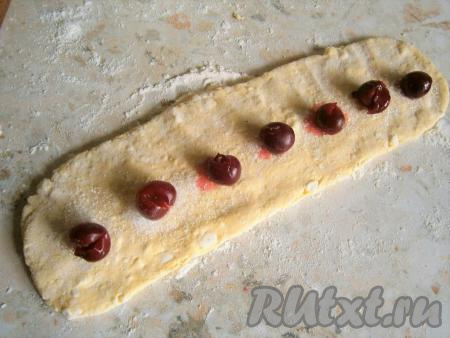 Если вишня замороженная, тогда разморозьте её и дайте стечь лишней жидкости. Из вишни удалить косточки. Тесто разделить на 2 части. Стол посыпать мукой. Каждую часть теста скатать в колбаску, а затем прижать скалкой (или руками). Ширина пласта теста должна быть, примерно, 8 см. Каждый раскатанный пласт теста посыпать по всей длине половиной столовой ложки сахара (сахар должен быть в виде тонкой полоски), затем на сахар выложить ягоды вишни на расстоянии 2-3 см.